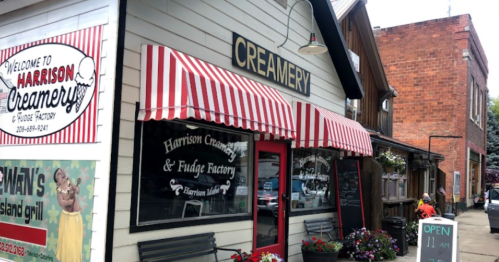 A charming creamery with red and white striped awnings, featuring a sign that reads "Harrison Creamery & Fudge Factory."