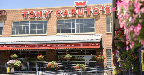 Exterior of Tony Caputo's market with colorful flower baskets and a clear blue sky.