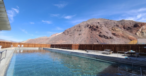 A serene pool surrounded by mountains under a clear blue sky, with wooden fencing in the background.