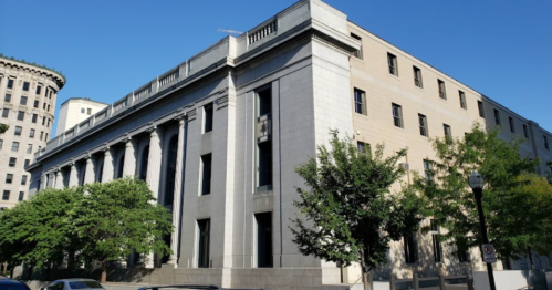 A large, modern building with columns and greenery, set against a clear blue sky.