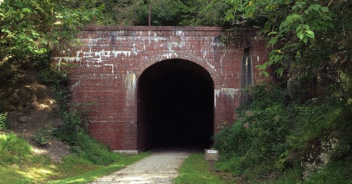 A dark brick tunnel surrounded by greenery, leading into a shadowy interior. A gravel path approaches the entrance.
