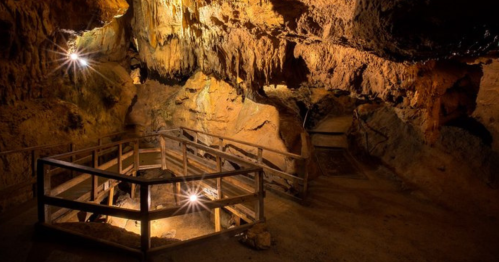 A dimly lit cave interior with wooden railings and rock formations, illuminated by soft lights.