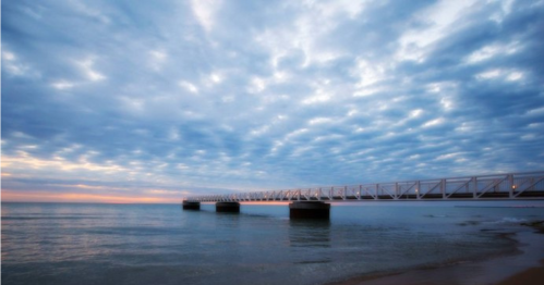 A serene view of a pier extending into calm waters under a cloudy sky at sunset.