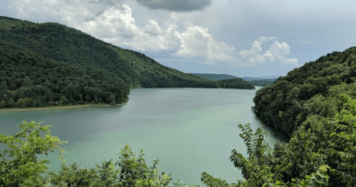 A serene lake surrounded by lush green hills under a cloudy sky.