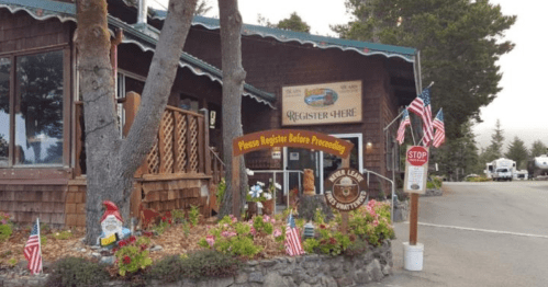 A rustic lodge entrance with a "Register Here" sign, surrounded by flowers and small American flags.