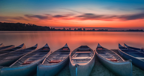 canoes sit on the sandy beach of Creve Couer lake in missouri at sunset