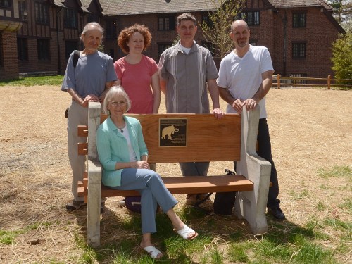 A group of five people poses together on a bench outside a building, smiling at the camera.