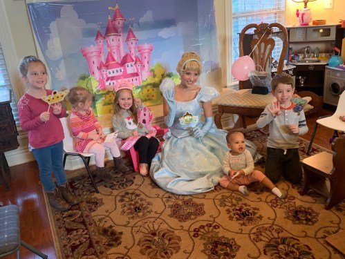 A group of children in costumes poses with a princess in a decorated room, celebrating a birthday or special event.