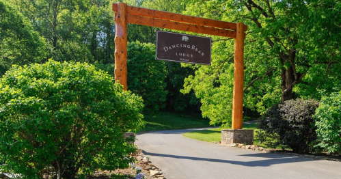 Wooden archway sign for Dancing Bear Lodge, surrounded by lush greenery and a winding driveway.