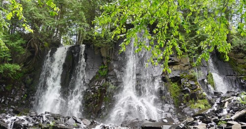 A serene waterfall cascading over rocky cliffs, surrounded by lush green foliage and trees.