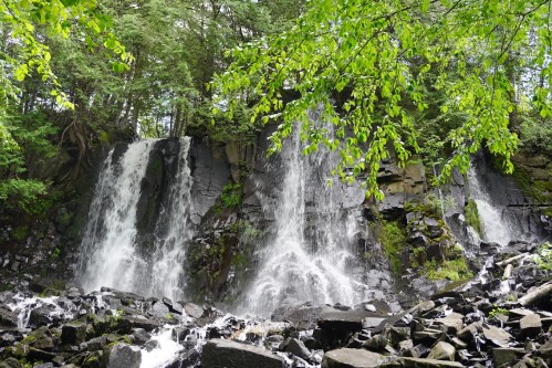 A serene waterfall cascading over rocky terrain, surrounded by lush green foliage and trees.