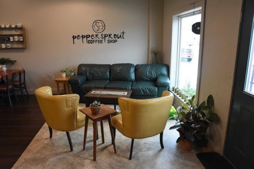 Cozy coffee shop interior with a green couch, yellow chairs, and plants, featuring a sign that reads "Peppersprout Coffee Shop."