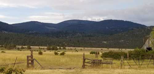 A scenic view of rolling hills and mountains, with a grassy field and wooden fences in the foreground.