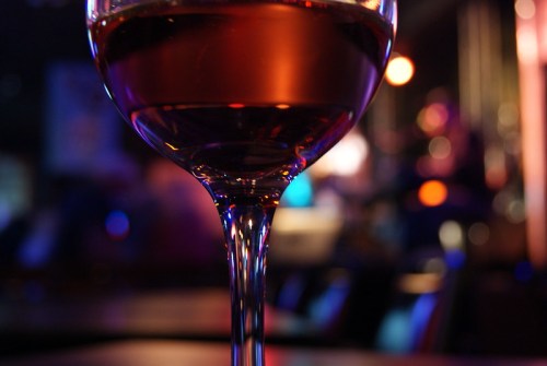 A close-up of a glass of red wine, with colorful blurred lights in the background.