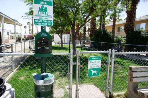 A fenced pet area with signs instructing to clean up after pets and a trash bin for waste disposal.