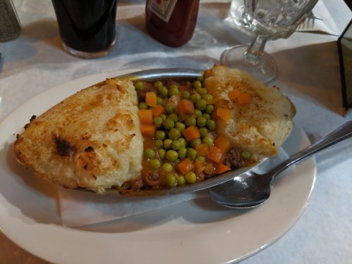 A metal dish with a meat and vegetable filling topped with two golden-brown potato dumplings, served on a white plate.