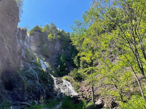 A scenic waterfall cascading down rocky cliffs, surrounded by lush green trees under a clear blue sky.