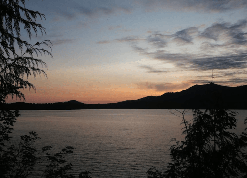 A serene lake at sunset, with silhouettes of trees and mountains against a colorful sky.
