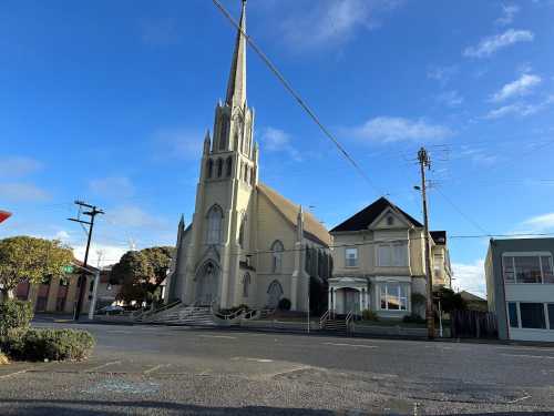 A tall church with a spire next to a large house, set against a clear blue sky and street view.