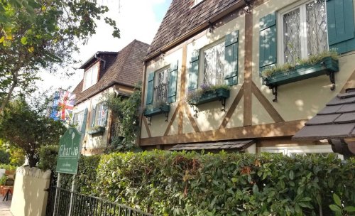 Charming cottage-style buildings with green shutters and a sign, surrounded by lush greenery and a British flag.
