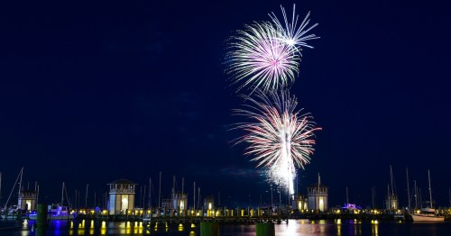 Colorful fireworks burst over a marina at night, illuminating the sky and reflecting on the water below.