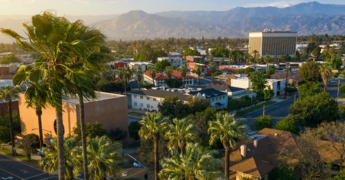 Aerial view of a city with palm trees, residential areas, and mountains in the background under a clear sky.