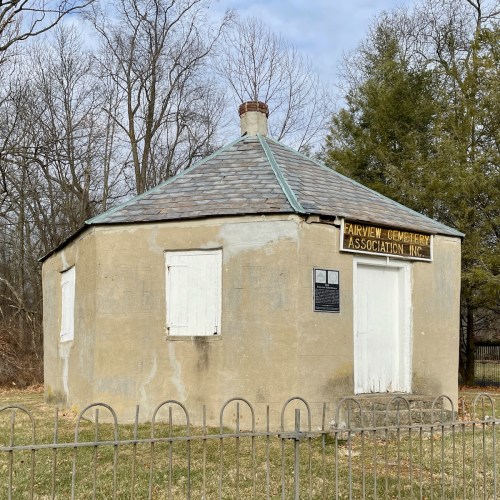 Round, weathered building with a slate roof and boarded windows, marked "Fairview Cemetery Association Inc." in a cemetery.