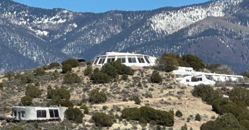 A modern, circular building on a hillside, surrounded by sparse vegetation and mountains in the background.