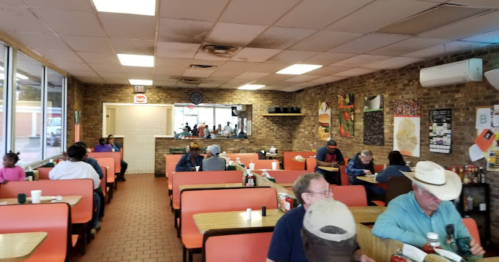A cozy diner with orange booths, patrons eating, and a brick wall adorned with art. A casual, welcoming atmosphere.