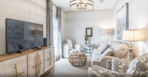 Cozy living room with a TV, light-colored sofas, a decorative table, and elegant curtains. Bright and inviting atmosphere.