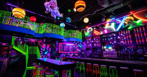 A vibrant, neon-lit bar with colorful decor, glowing planets, and a unique space-themed atmosphere.
