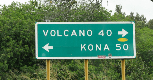 Green highway sign indicating directions to Volcano (40 miles) and Kona (50 miles) with arrows pointing left and right.