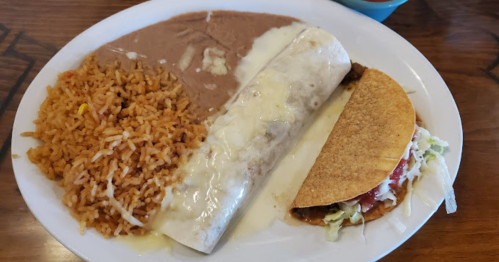 A plate featuring rice, refried beans, a cheese-covered burrito, and a taco with lettuce and tomato.