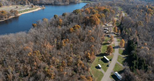 Aerial view of a river surrounded by autumn trees and a campground with RVs along a winding road.