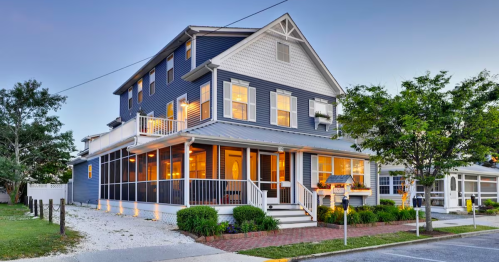 A large blue house with a porch, multiple windows, and a well-kept yard, illuminated at dusk.