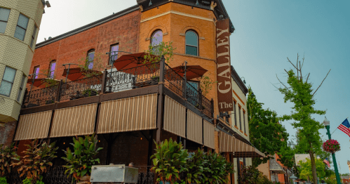 A historic building with a sign reading "The Galley," featuring outdoor seating and lush greenery.