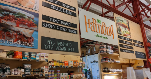 A vibrant deli display featuring vegan sandwiches and a menu board at a plant-based eatery.