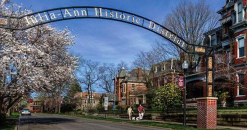 Archway sign for the Julia-Ann Historic District, with blooming trees and people walking a dog on a sunny day.
