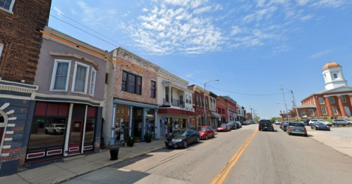 A charming street lined with historic buildings, shops, and parked cars under a clear blue sky.
