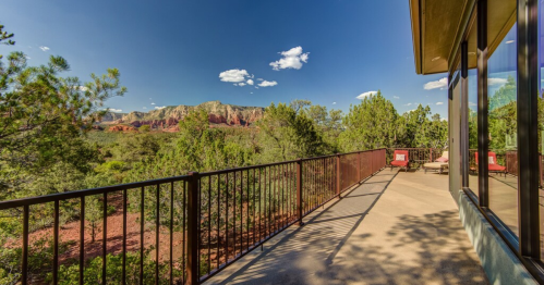 A scenic view from a balcony overlooking lush greenery and red rock formations under a clear blue sky.