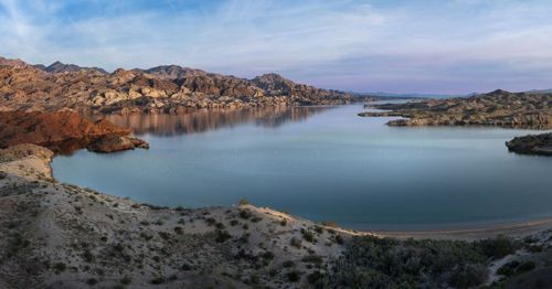 A serene landscape featuring a calm lake surrounded by rocky mountains and sandy shores under a clear sky.