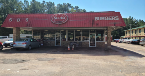 A roadside burger restaurant with a red roof and large windows, surrounded by parked cars and trees.