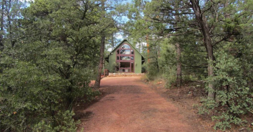 A green cabin surrounded by trees, with a gravel path leading up to it.