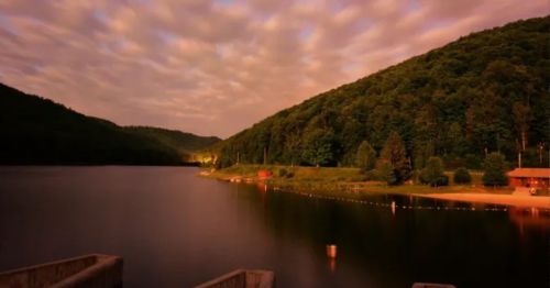 A serene lake surrounded by lush green hills under a cloudy sky at dusk.