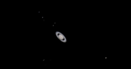 A detailed view of Saturn with its iconic rings, set against a black background, showcasing several surrounding moons.
