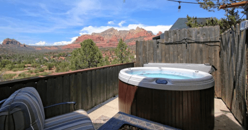 A hot tub on a patio with a scenic view of red rock formations and trees under a blue sky.