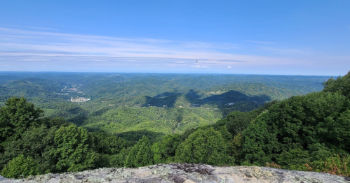 A panoramic view of lush green mountains under a clear blue sky, with distant hills and valleys visible.