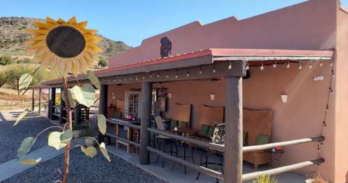A rustic building with a sunflower sculpture in front, featuring outdoor seating and a mountain backdrop.
