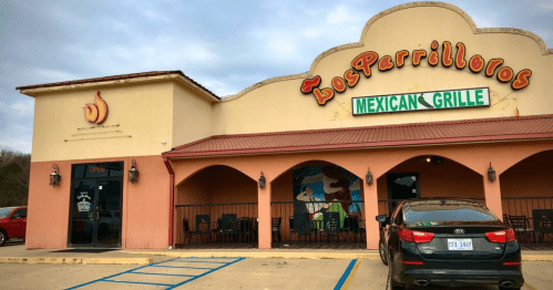 Exterior of Los Parrilleros Mexican Grille, featuring a colorful sign and outdoor seating area. A car is parked nearby.