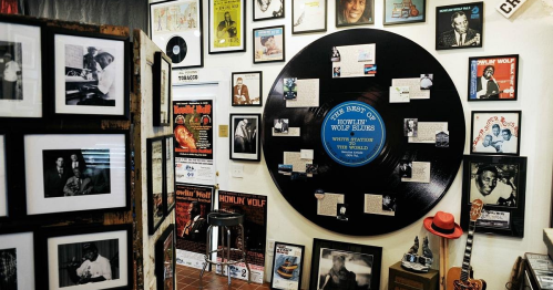 A wall decorated with framed photos, records, and posters, featuring a large vinyl record at the center.